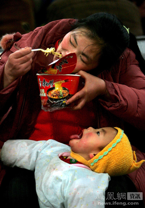 2006年1月18日，北京西客站候车室，一位母亲咬断方便面喂孩子，而她的孩子早等不及地张大了嘴巴。薛�B/摄