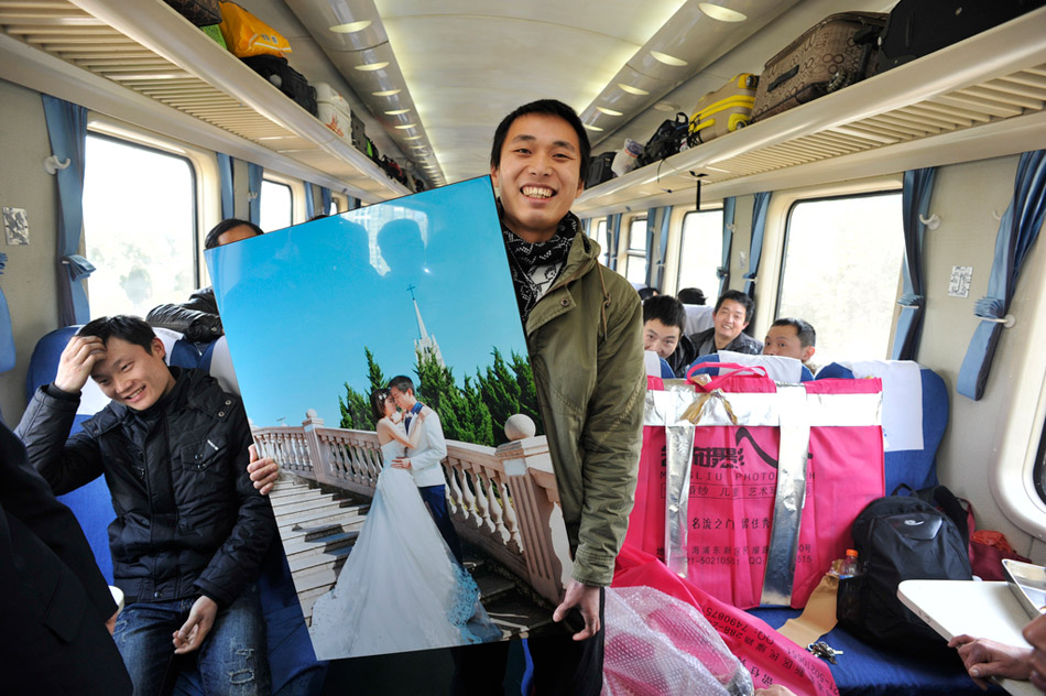 2016年1月25日，上海到成都列车上，唐军千里扛回家的神秘物件，是他和未婚妻拍摄的婚纱照。这是一趟暖意浓浓的四川人回家列车。在数百位四川老乡的欢呼声中，这位腼腆的小伙子写下新年祝愿，当着全车厢的人面喊出未婚妻的名字，大声说：等我回来娶你。陈羽啸/华西都市报/视觉中国
